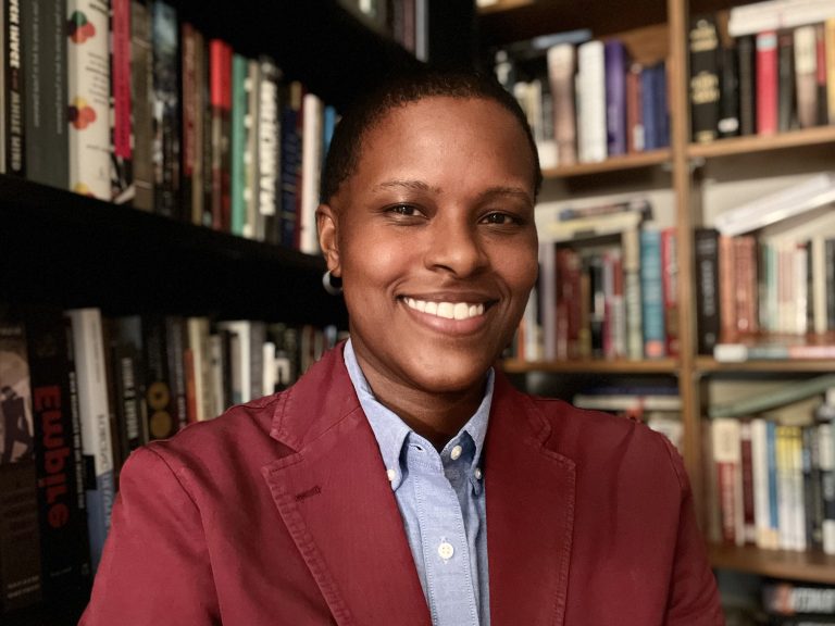 Brittney Edmonds in front of shelved books smiling and wearing a maroon blazer