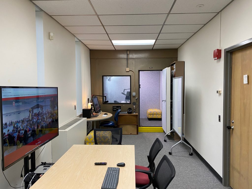 A table and monitor, recording booth in the background