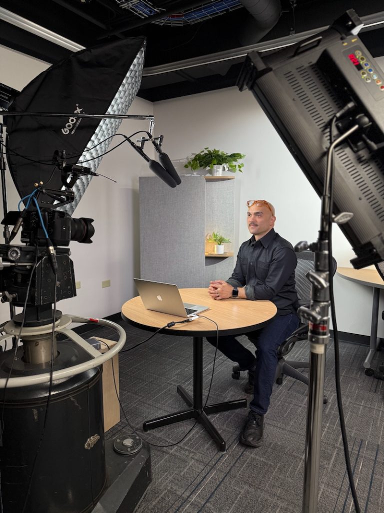 A table and chair in a video studio with a bright light, camera in the foreground.