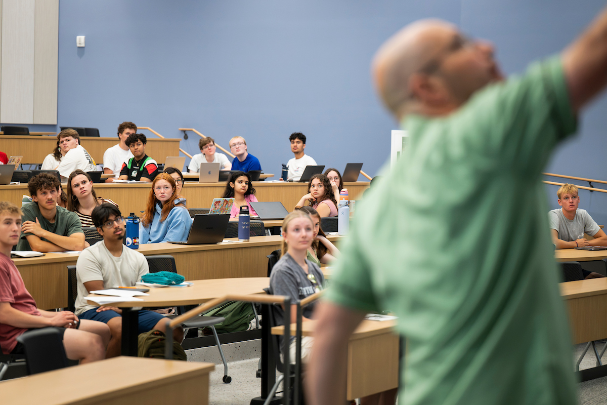 Students listen and watch an instructor making notes during a history lecture